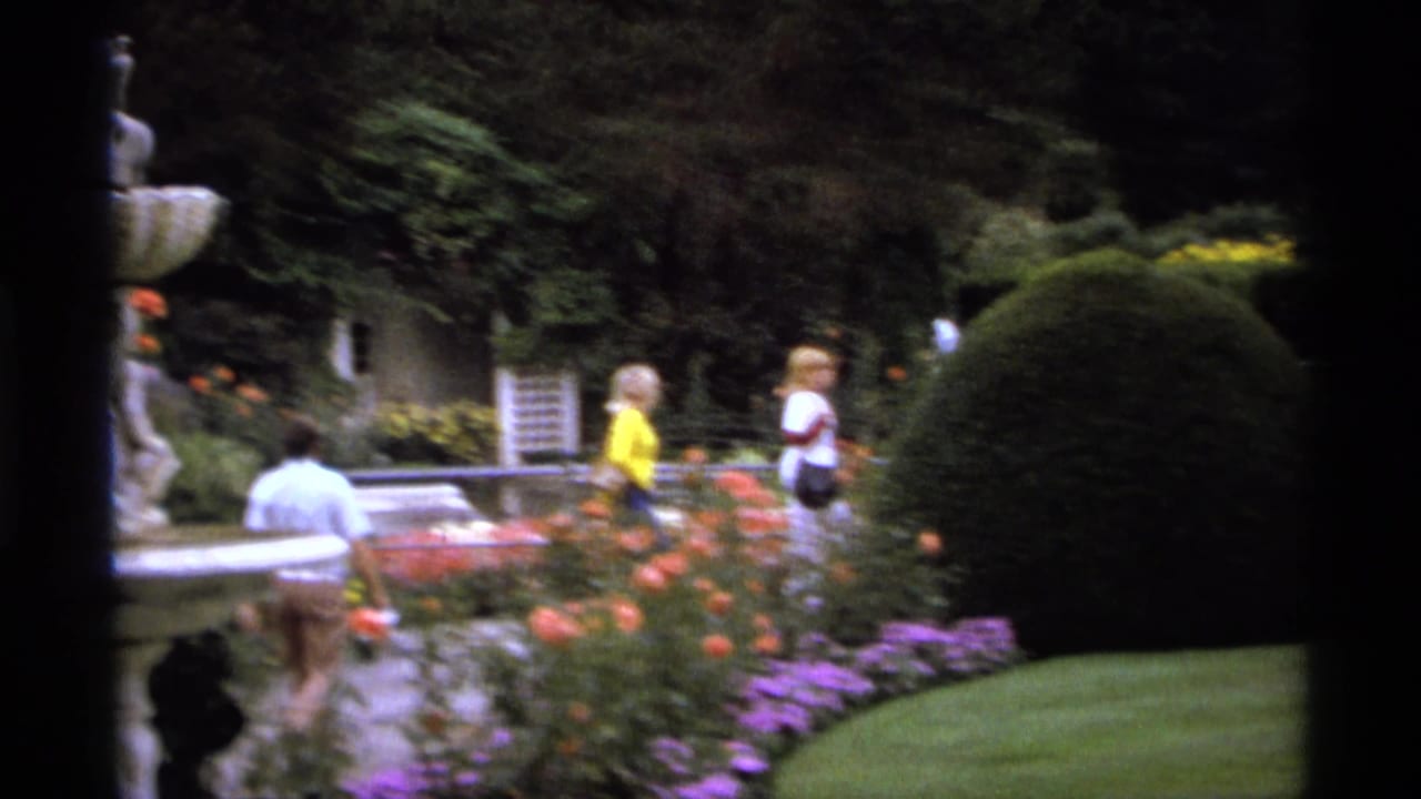 Visitors walk through flowerbeds near a fountain and clipped hedges in a garden.