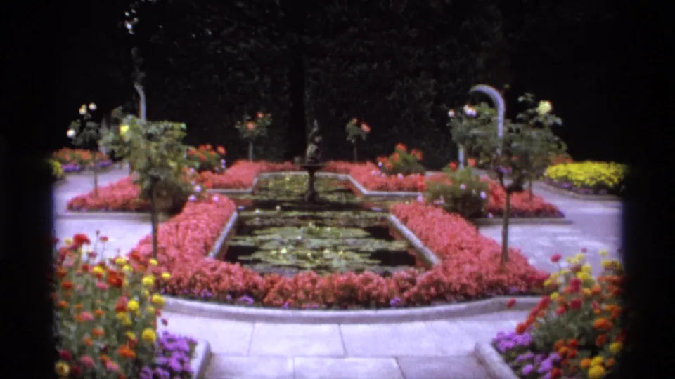 1974 Vancouver garden footage shows a rectangular pond or fountain basin with lily pads, pink borders, paved paths, and surrounding flowers.