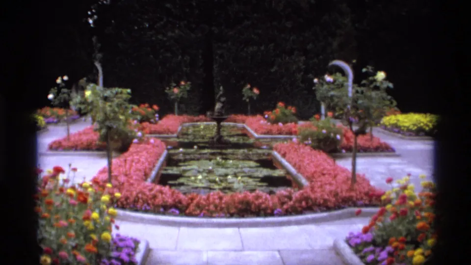The 1974 Vancouver park garden view centers on a pond or fountain basin surrounded by pink planting beds, paths, and mixed flowers.