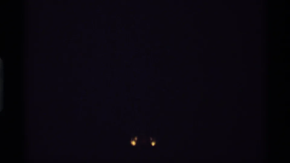 Near-black 1974 8mm frame with two small glowing points low in the image and visible film grain at the end of the clip.