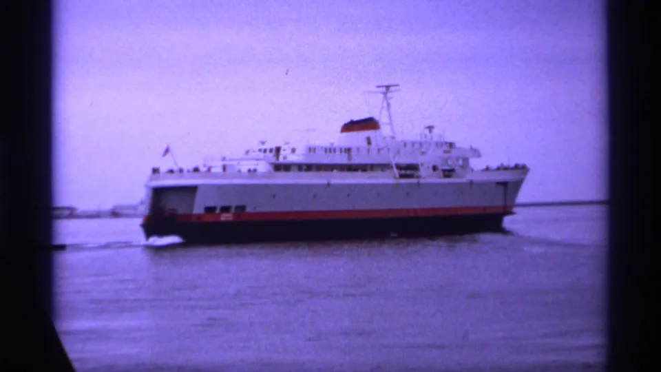 1974 Vancouver-area 8mm view of a white multi-deck ferry with a red stripe crossing calm harbor water.