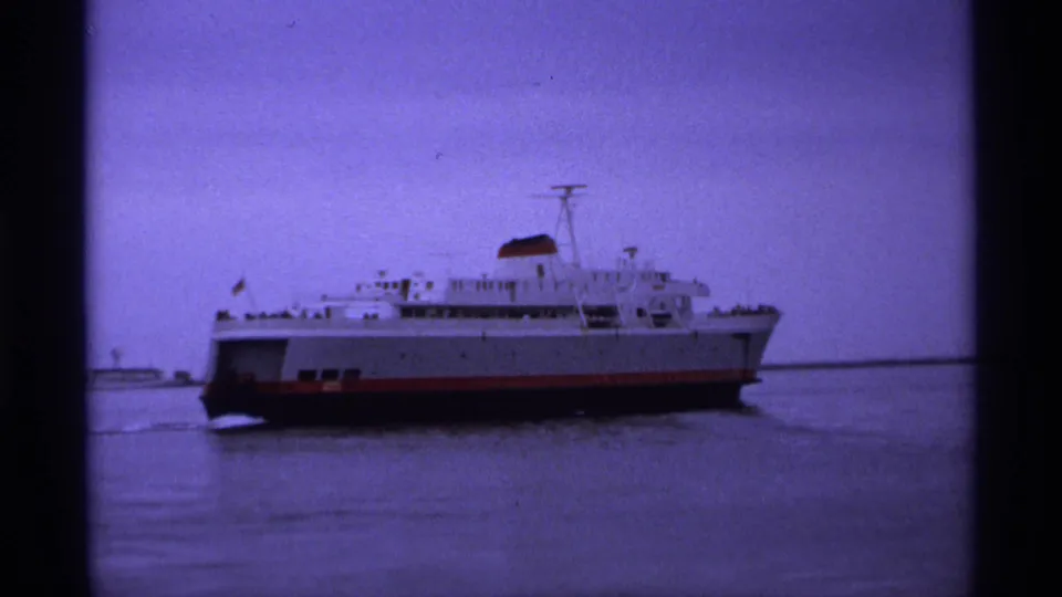 The ferry remains in view on calm water, with soft focus, visible grain, and purple color shift from the aged 8mm film scan.