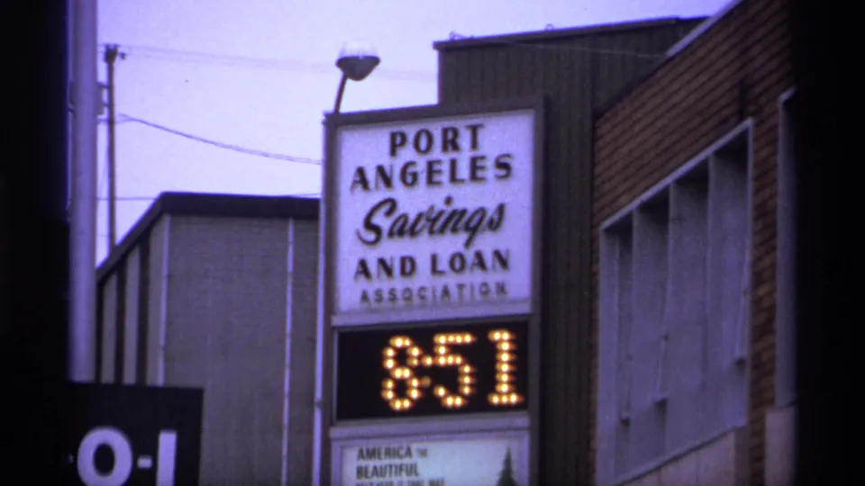 A street-level 8mm frame shows a Port Angeles Savings and Loan Association sign, brick building walls, utility lines, and a digital display reading 851.