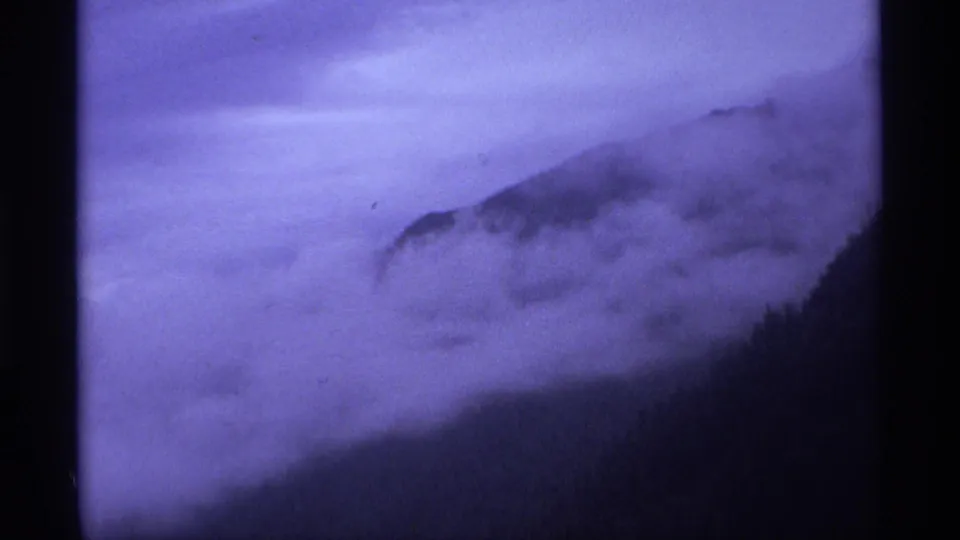 1974 Vancouver-area landscape frame showing a fog-covered mountainside in soft purple-tinted 8mm color.
