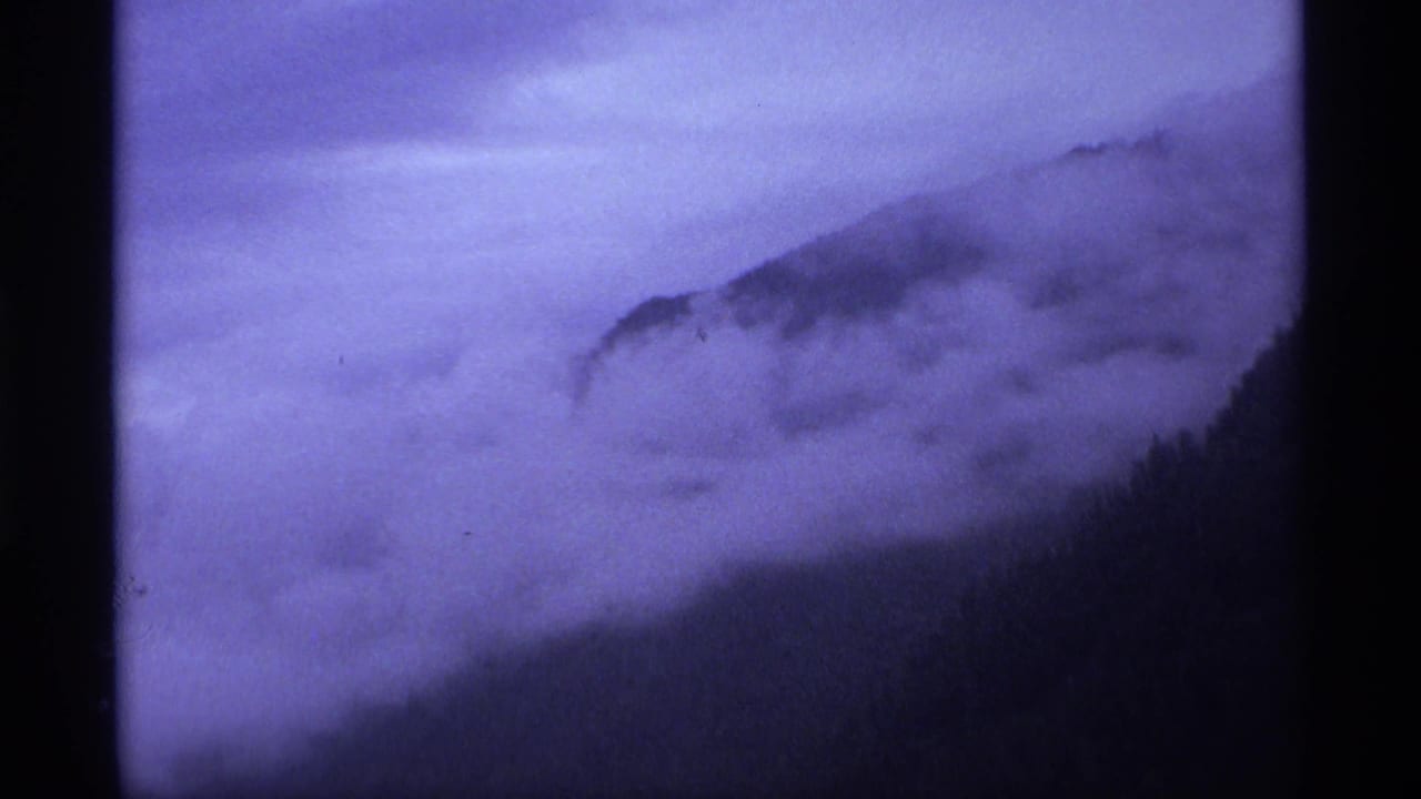 1974 Vancouver-area 8mm frame showing fog blanketing a dark tree-covered hill under a violet twilight sky.