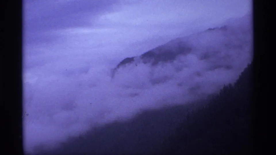 1974 Vancouver-area 8mm frame showing fog blanketing a dark tree-covered hill under a violet twilight sky.