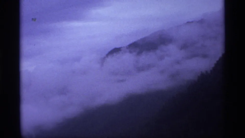 1974 Vancouver-area 8mm frame with a mist-covered ridge, dark wooded slope, and soft purple-blue exposure.