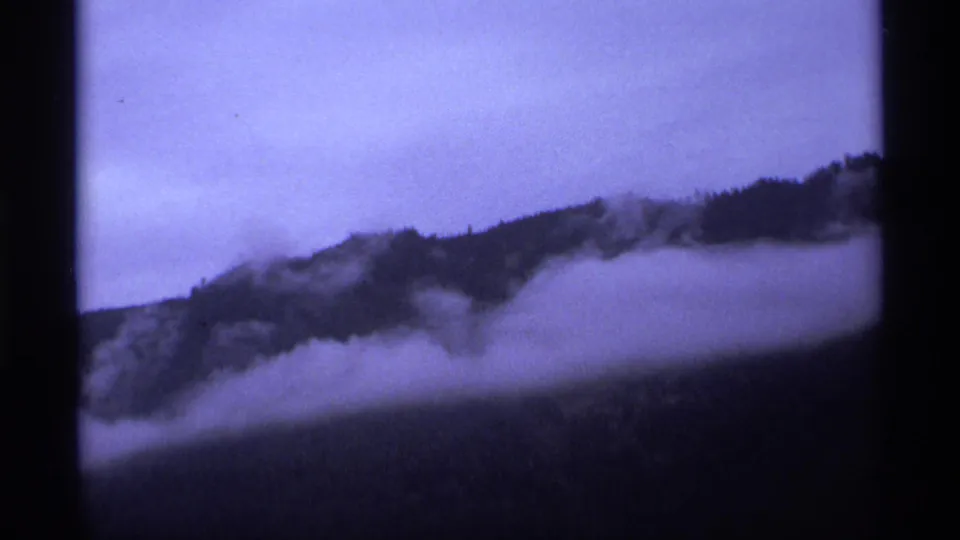 1974 Vancouver-area 8mm frame showing low fog wrapped around a long forested ridge in fading light.