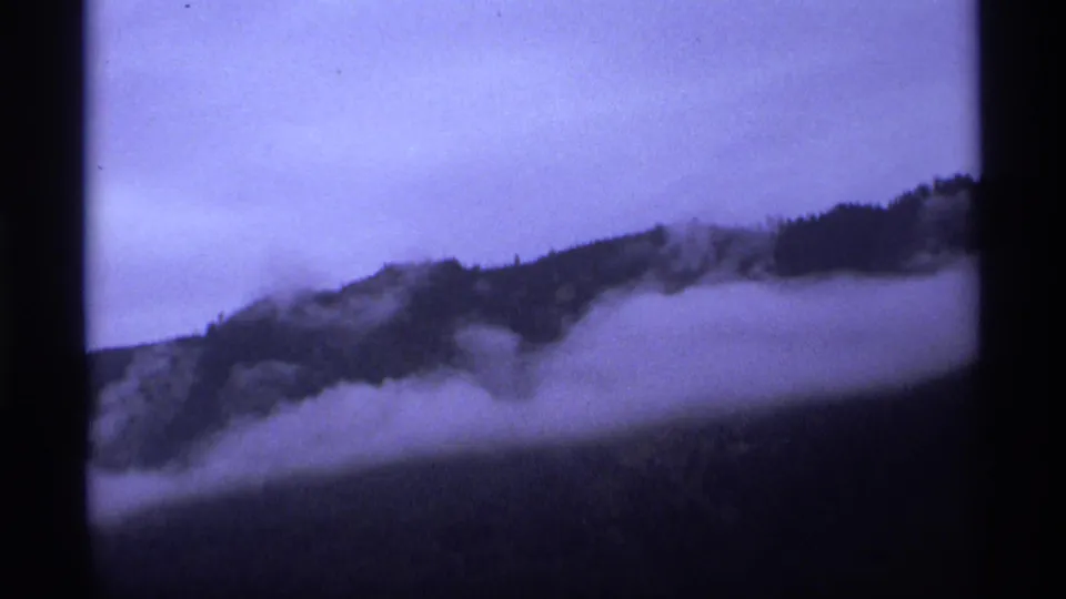 1974 Vancouver-area 8mm frame with a dark forested ridge emerging from fog beneath a muted twilight sky.
