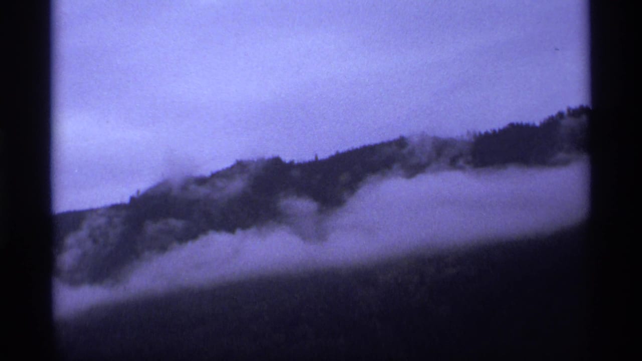 Misty dark mountain slopes under low cloud, framed by black film borders.