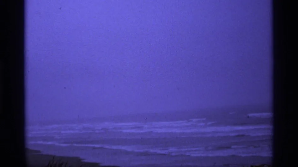 Vintage 8mm seascape showing purple-tinted sky, distant surf, and a dark foreground shoreline near Vancouver per clip metadata.