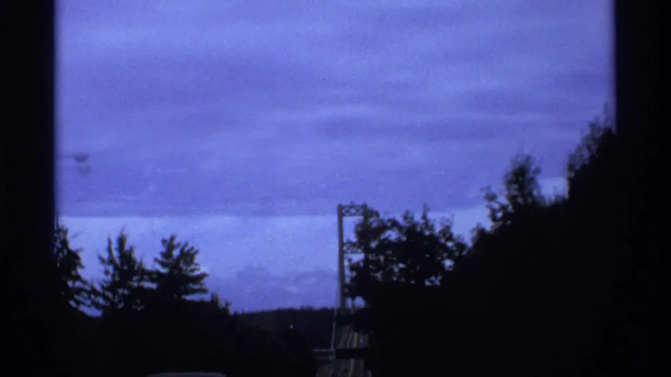 Moving 8mm travel view near Vancouver with a suspension bridge tower partly obscured by silhouetted trees.
