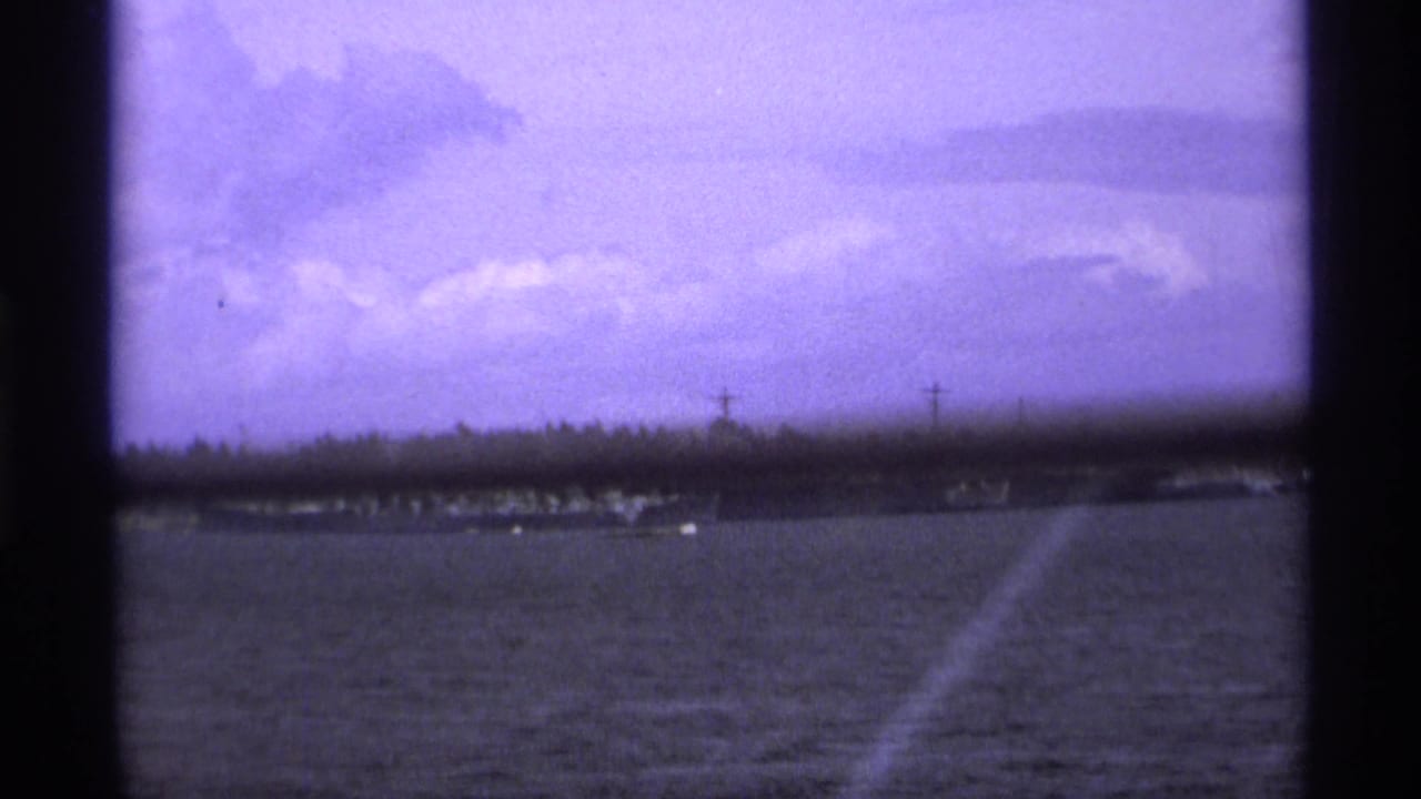 Distant naval ship on water beneath cloudy sky, seen through dark 8mm frame edges.