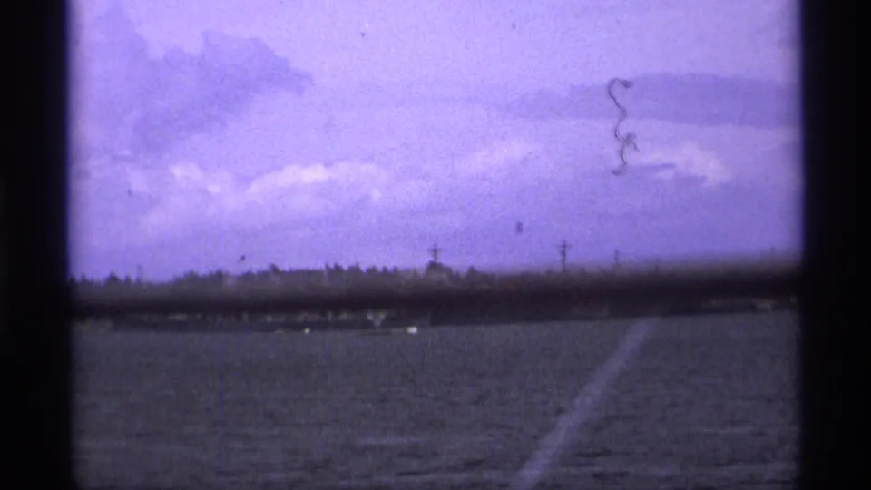 Distant military vessel near the Vancouver shoreline, framed by cloudy sky, 8mm borders, and visible film wear.