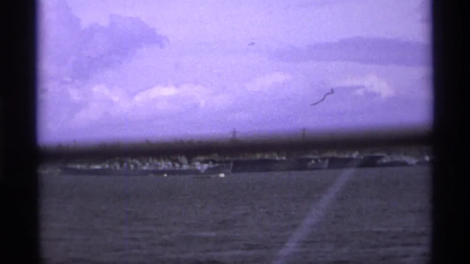 Wide 1974 Vancouver harbor view with a distant military ship, low shoreline, cloudy sky, and soft purple 8mm exposure.