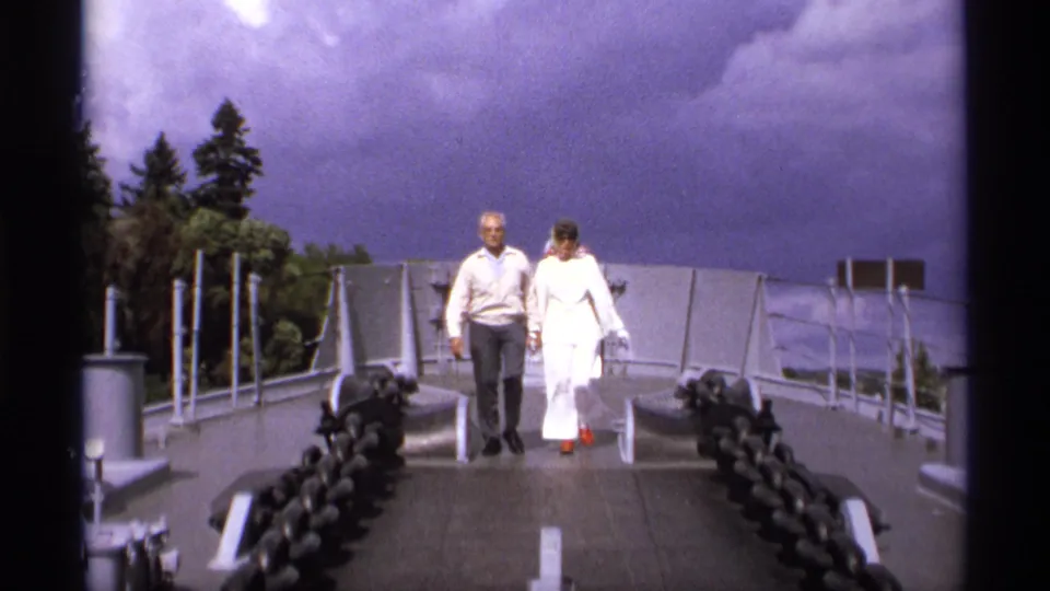 1974 Vancouver home-movie frame showing an elderly couple approaching on a bridge walkway under a cloudy sky.