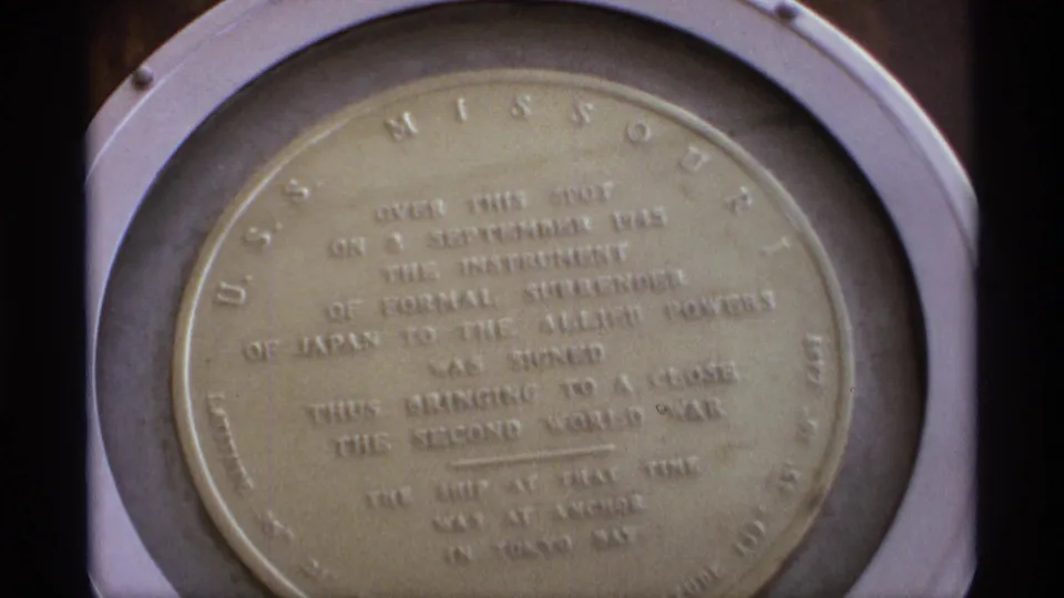 1974 Vancouver 8mm frame showing a round USS Missouri commemorative plaque with surrender text, filmed close from a visitor angle.