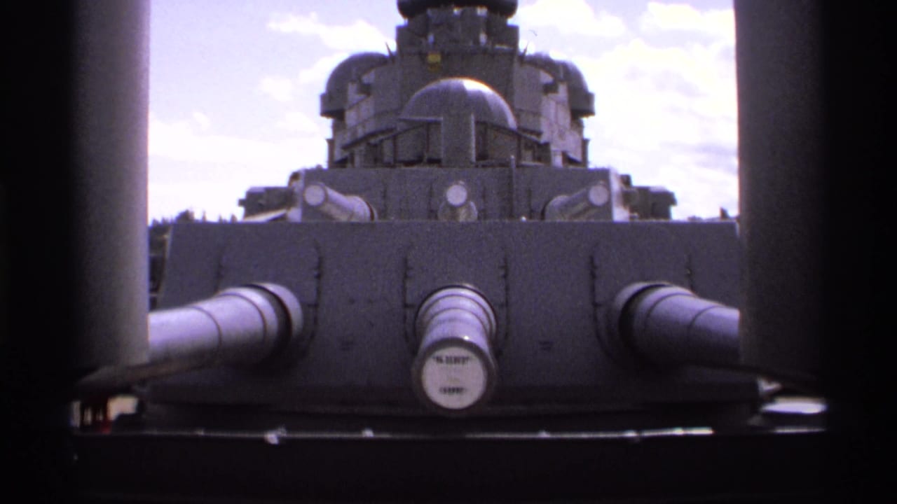 Large gray naval gun turret seen between dark vertical deck structures.