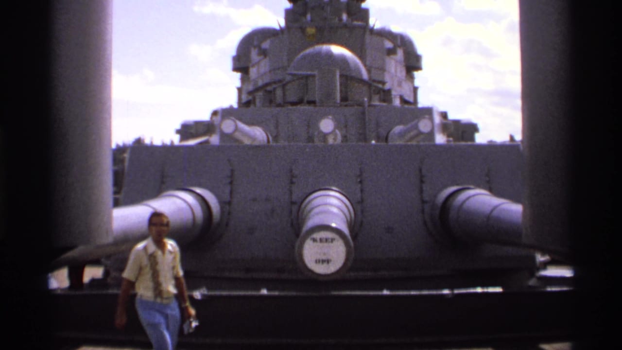 Man walks in front of a gray naval gun turret and large gun barrels.