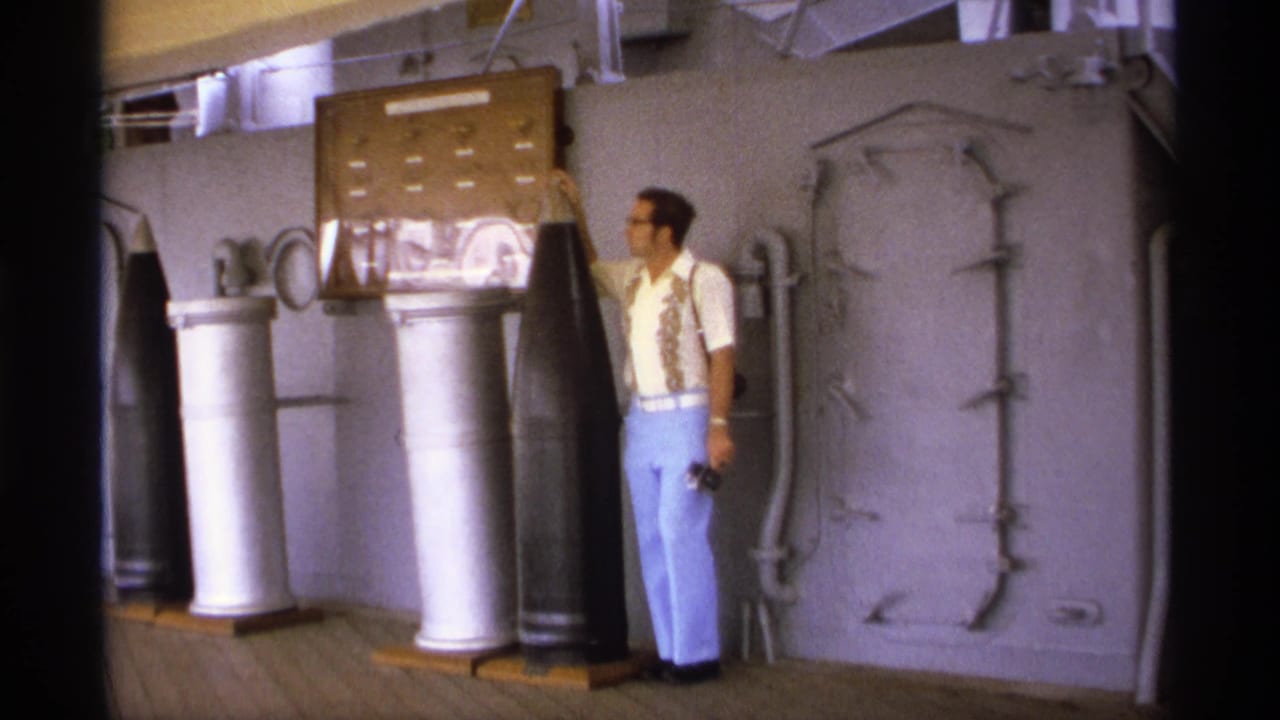 Man standing beside large naval ordnance on a ship deck.
