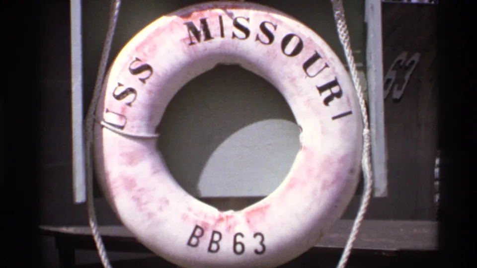 Close-up of a life ring marked USS Missouri BB 63 hanging against dark ship structure with rope visible at the sides.