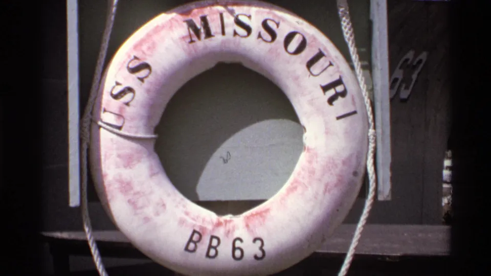 Close 1974 Vancouver 8mm view of a weathered USS Missouri BB63 life ring with rope and dark ship structure behind it.