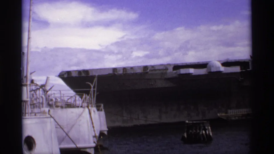 Wide 8mm harbor view of USS Missouri docked in Vancouver, with gray hull, pier railings, water, and cloudy sky visible.