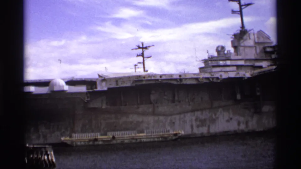 1974 Vancouver 8mm view of a weathered gray warship hull and island structure docked in a shipyard-like waterfront setting.