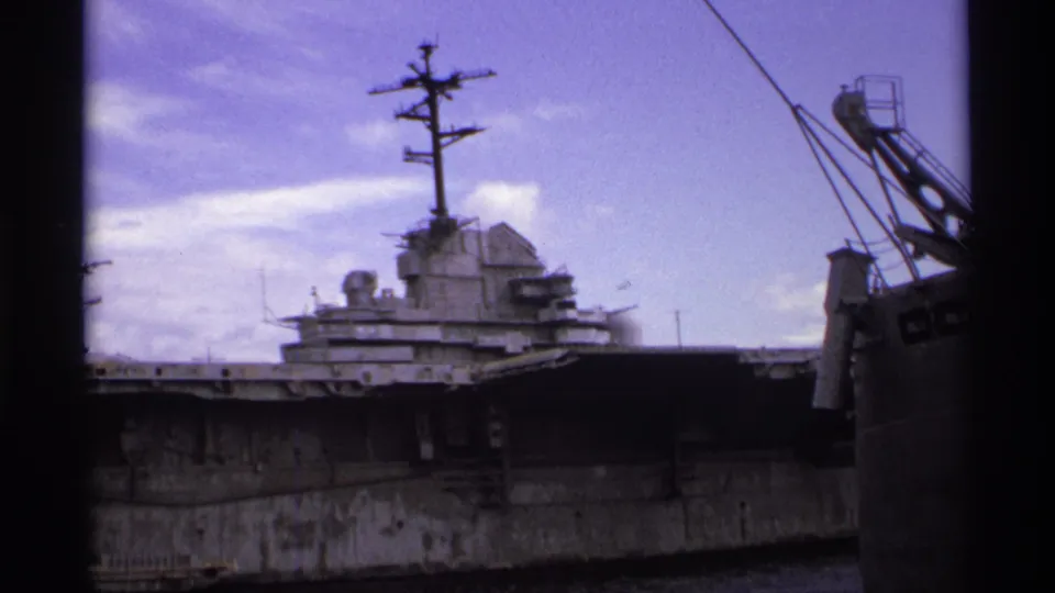 1974 Vancouver shipyard view of a docked warship with flight deck, island structure, mast, crane, and visible 8mm framing.