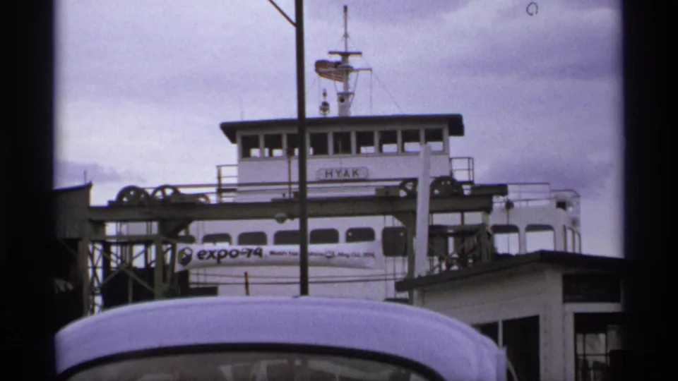1974 ferry dock view with the HYAK bridge and Expo 74 banner visible, framed by dark foreground edges and cloudy sky.