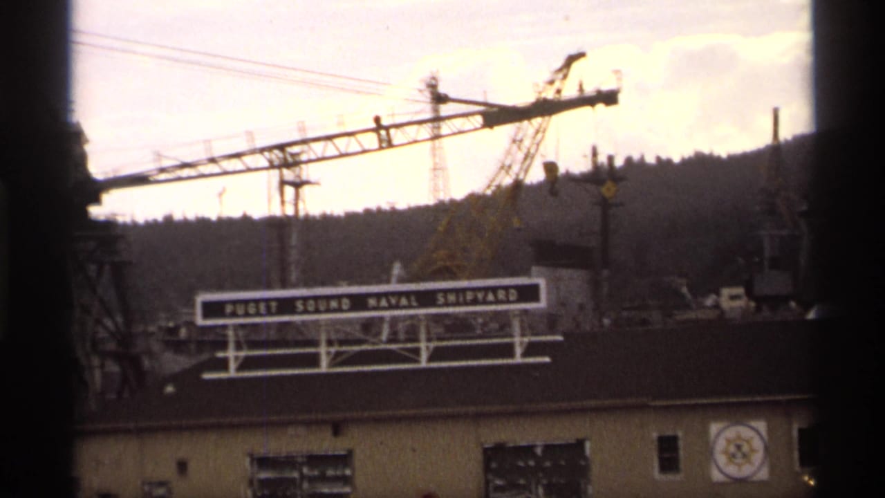 Closer view of the shipyard sign, cranes, and waterfront building.