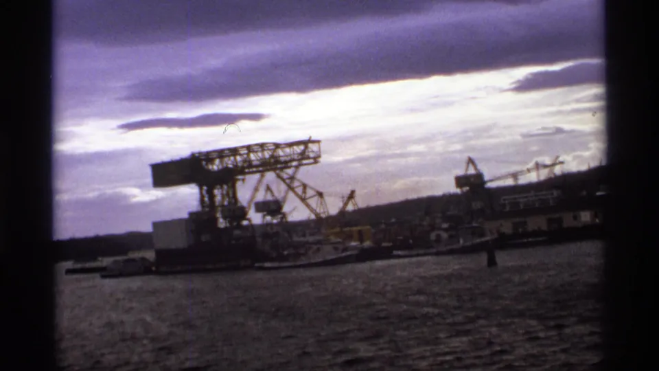 Vancouver harbor footage from 1974 showing cranes, water, shoreline structures, distant hills, and a dark film-frame edge.