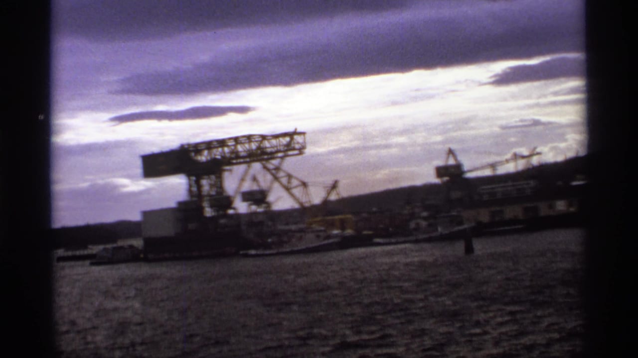 Industrial waterfront with cranes beside a river under a cloudy sky.