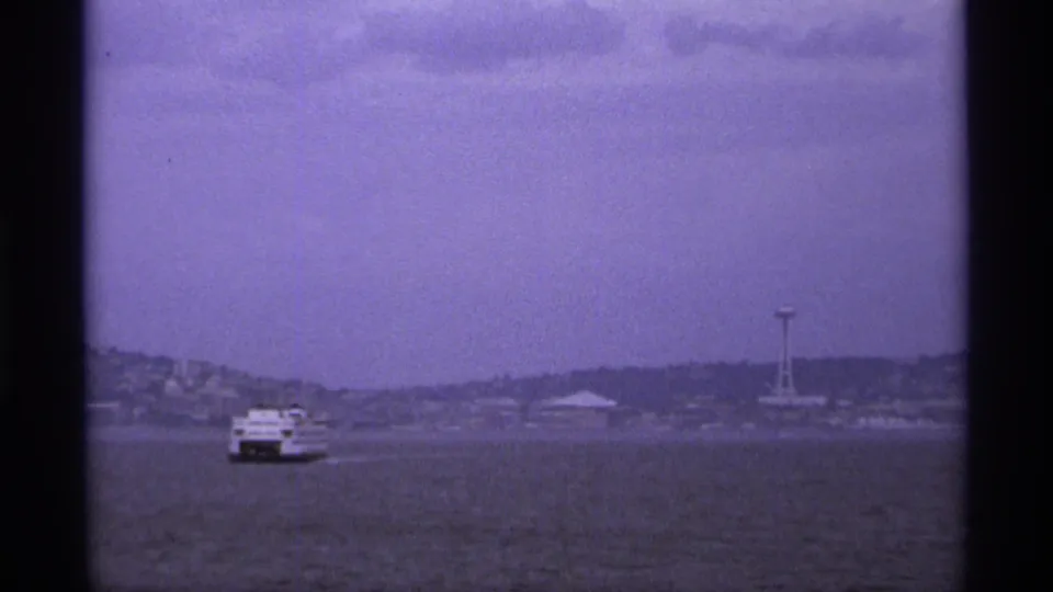 The ferry appears farther across the water, with hazy shoreline buildings and a needle-like observation tower in the distance.