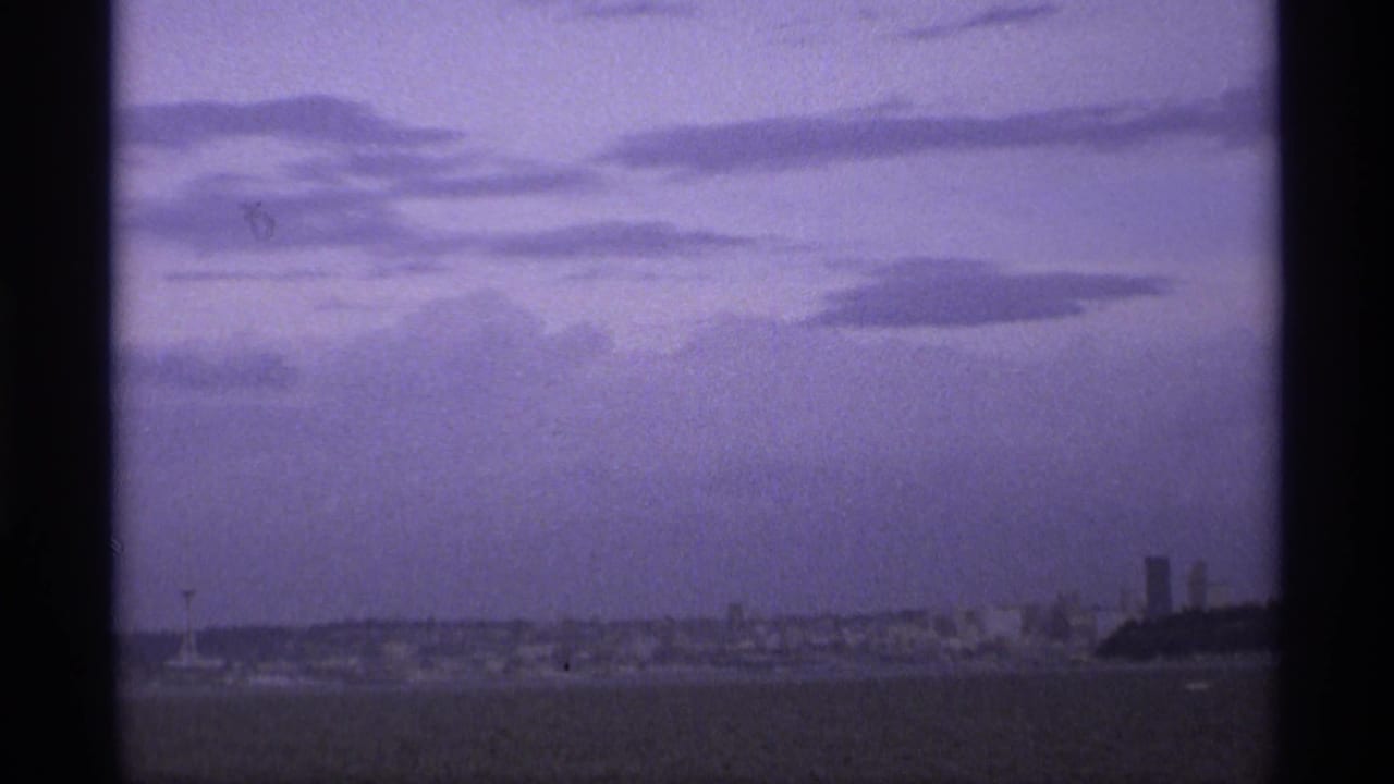 Storm clouds over water with a distant waterfront skyline and dark film-frame edges.