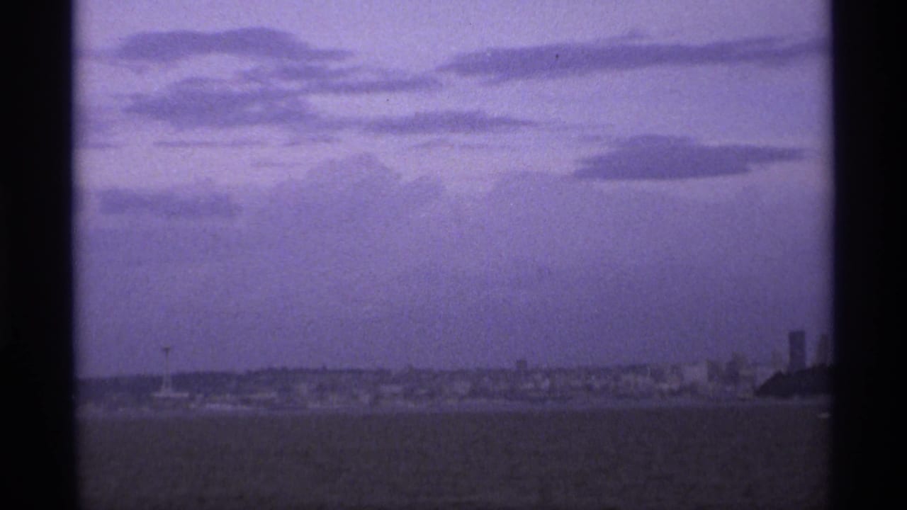 Distant waterfront under layered clouds, viewed through dark vertical film-frame borders.