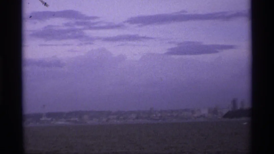 Soft 8mm view of Vancouver water and a distant shoreline beneath broad storm clouds, with visible frame borders and color shift.