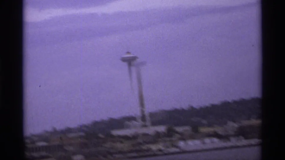 Closer 1974 8mm view of an observation tower rising above a waterfront area and dark hillside, with visible blur and color shift.