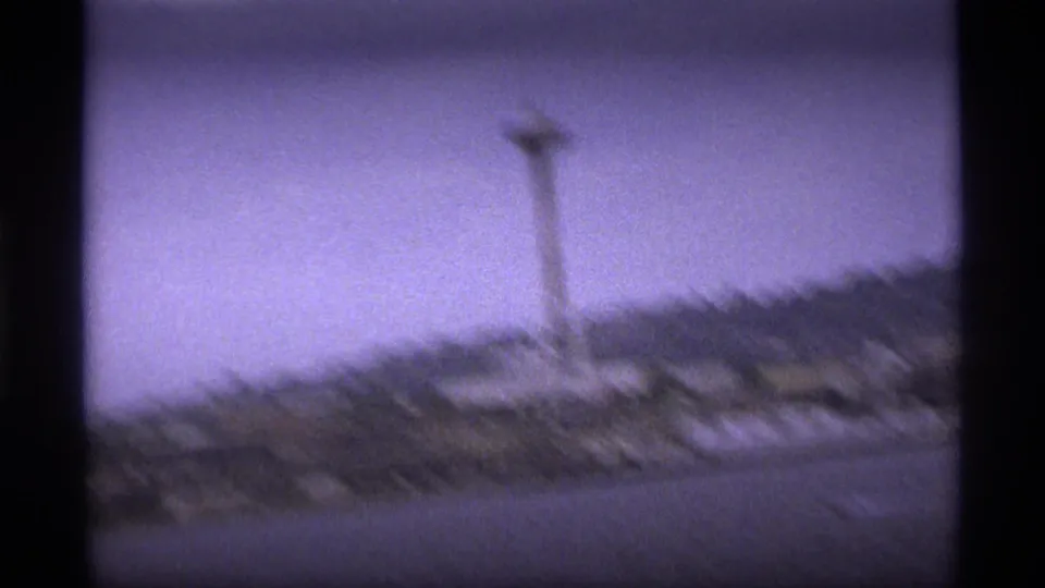 Soft, shaky 8mm frame where the Space Needle appears blurred above the waterfront and hillside under a pale sky.