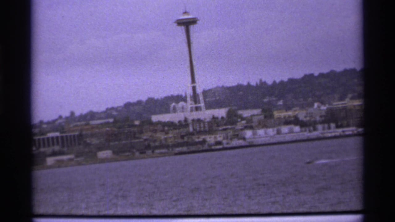 Space Needle above waterfront buildings across open water under a cloudy sky.