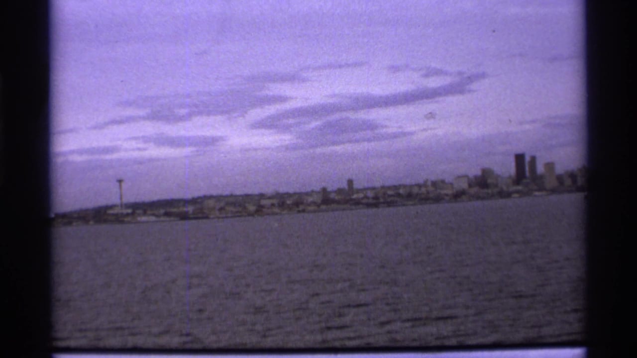 Distant skyline across water with a needle-like tower and dark 8mm frame borders.