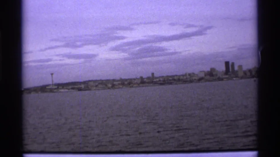 1974 8mm frame showing the Vancouver skyline from across the water, with clustered towers and a low horizon.