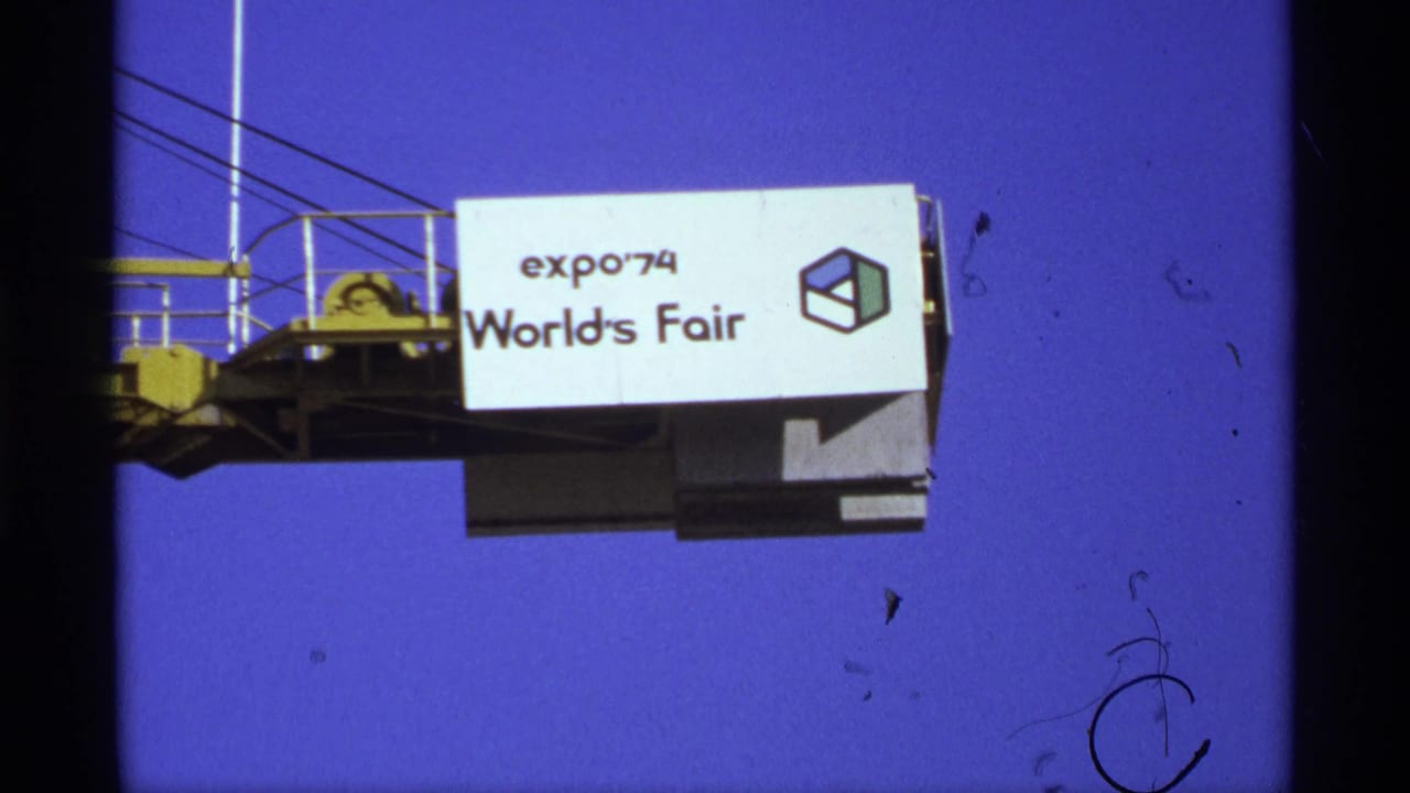 Expo '74 World's Fair sign mounted on a yellow crane arm against blue sky.
