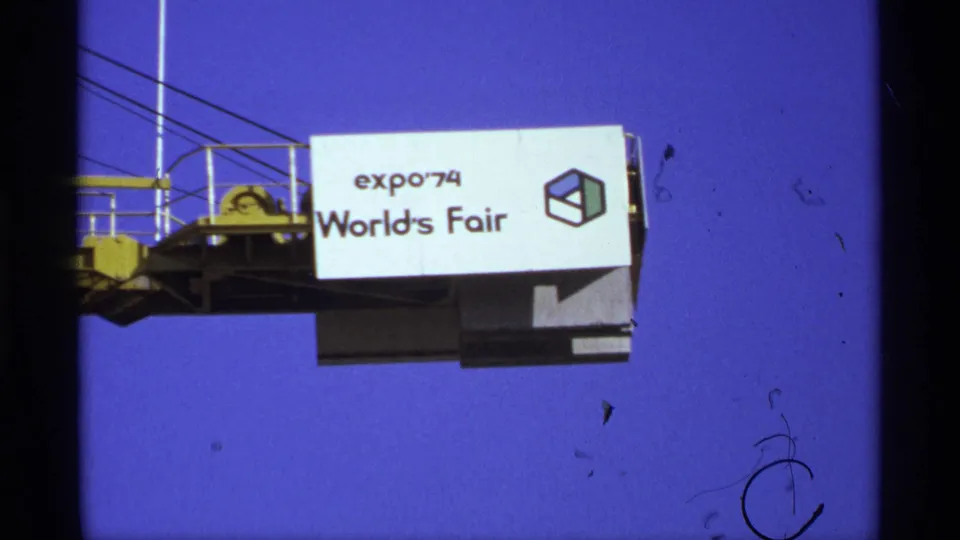 1974 8mm frame showing an Expo '74 World's Fair sign on a yellow crane arm, with cables and deep blue sky visible.