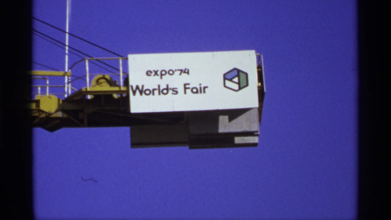 Expo '74 World's Fair sign and cube logo on a crane arm against clear blue sky.