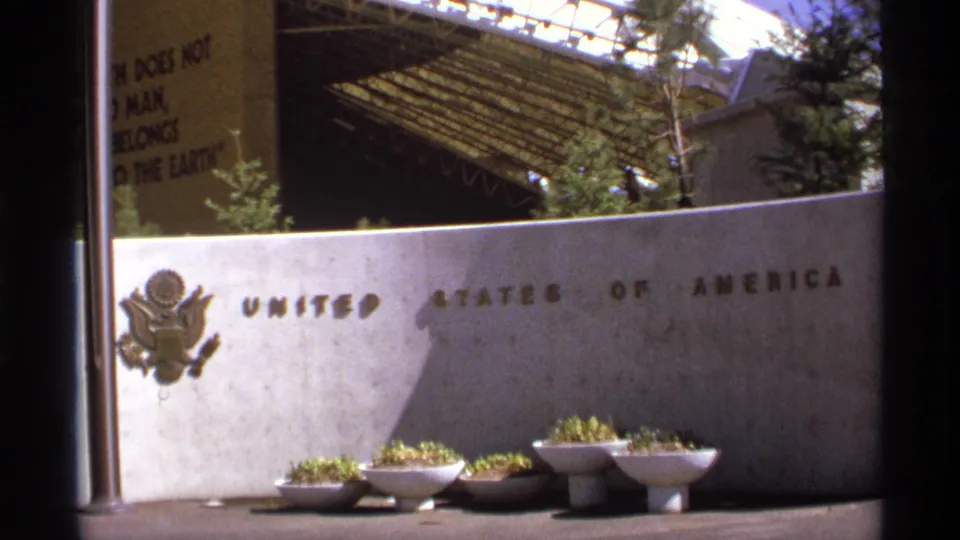 1974 8mm frame showing the United States of America wall inscription, U.S. seal, planters, and fair pavilion structure.