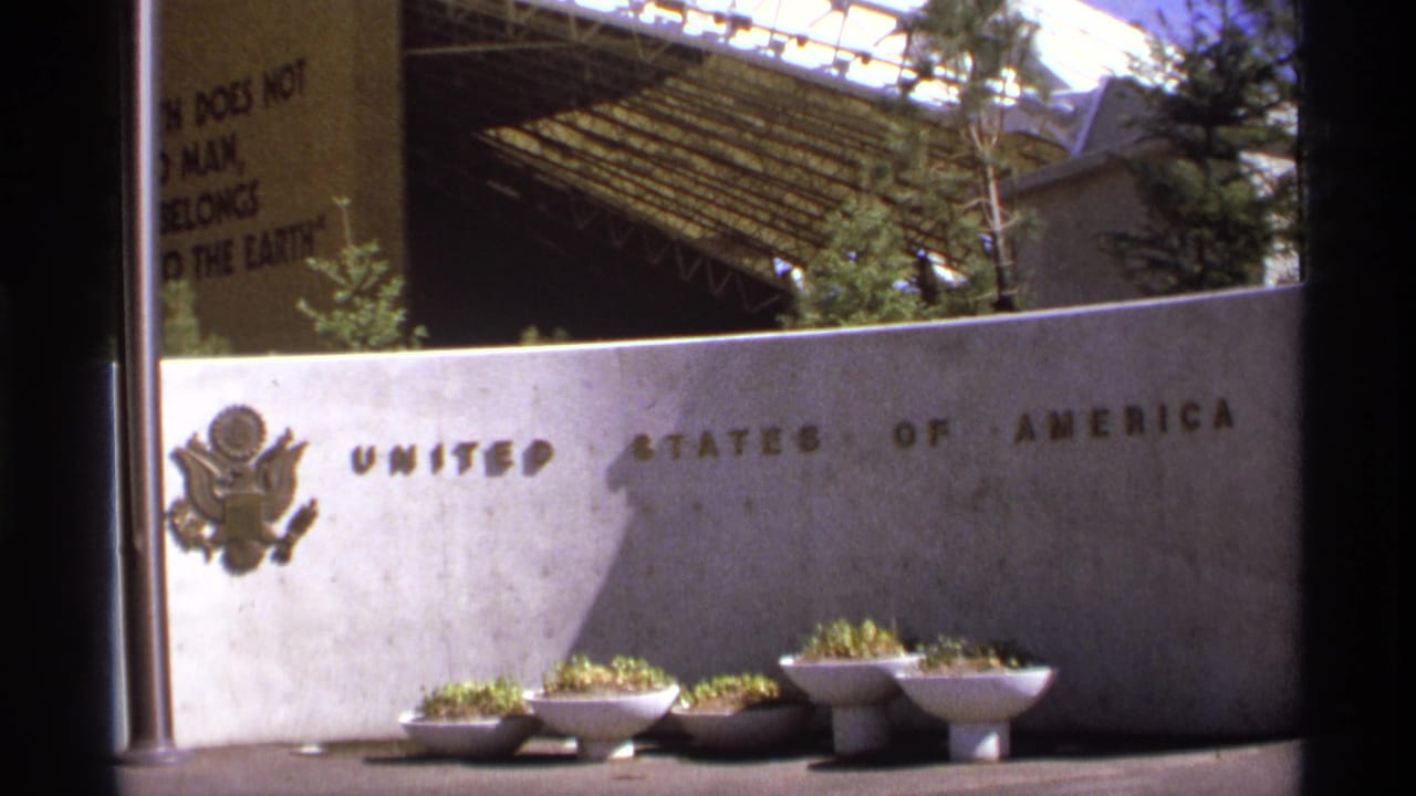 Concrete United States of America sign with U.S. seal and white planters beneath an arched structure.