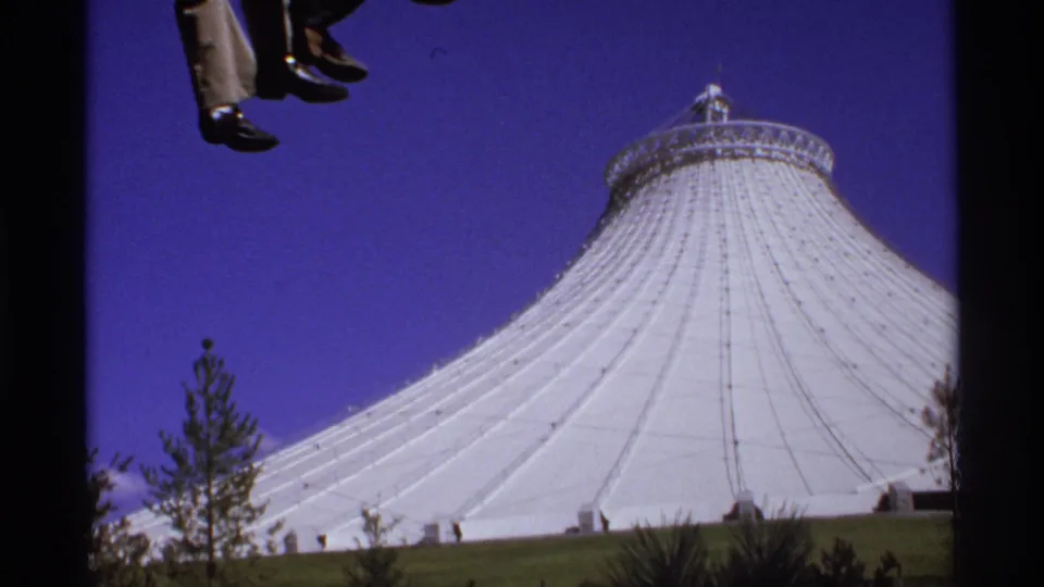 Visitor-shot 8mm view from a ride, with dangling feet at the top of frame and a white Seattle dome identified by metadata below.