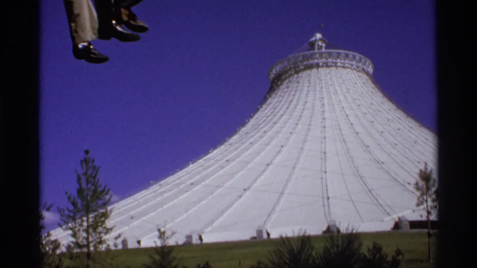 8mm ride POV showing a large white dome and landscaped grounds, with suspended feet clipped at the top of the frame.