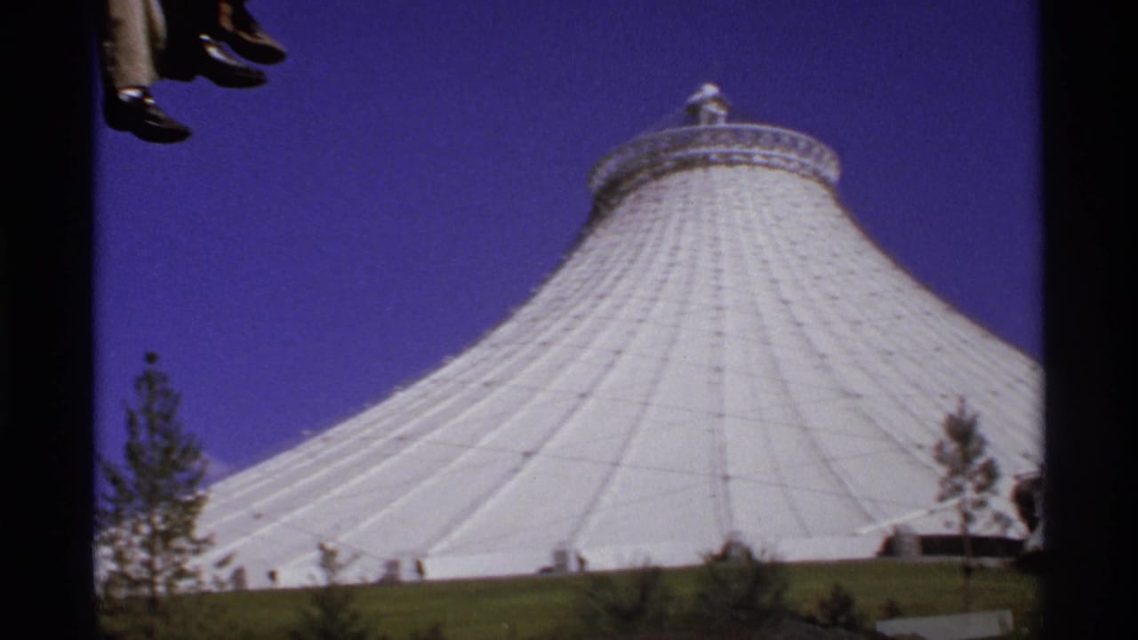 White tent-like pavilion under a deep blue sky with part of an aerial car at the top edge.